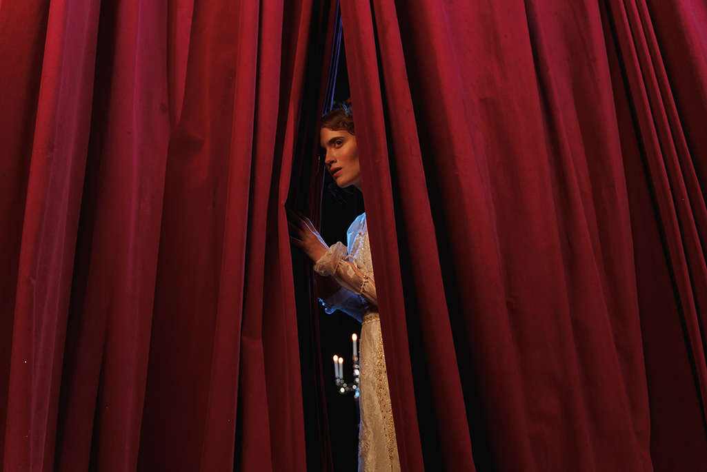En kvinna tittar fram genom ett draperi på en scen.