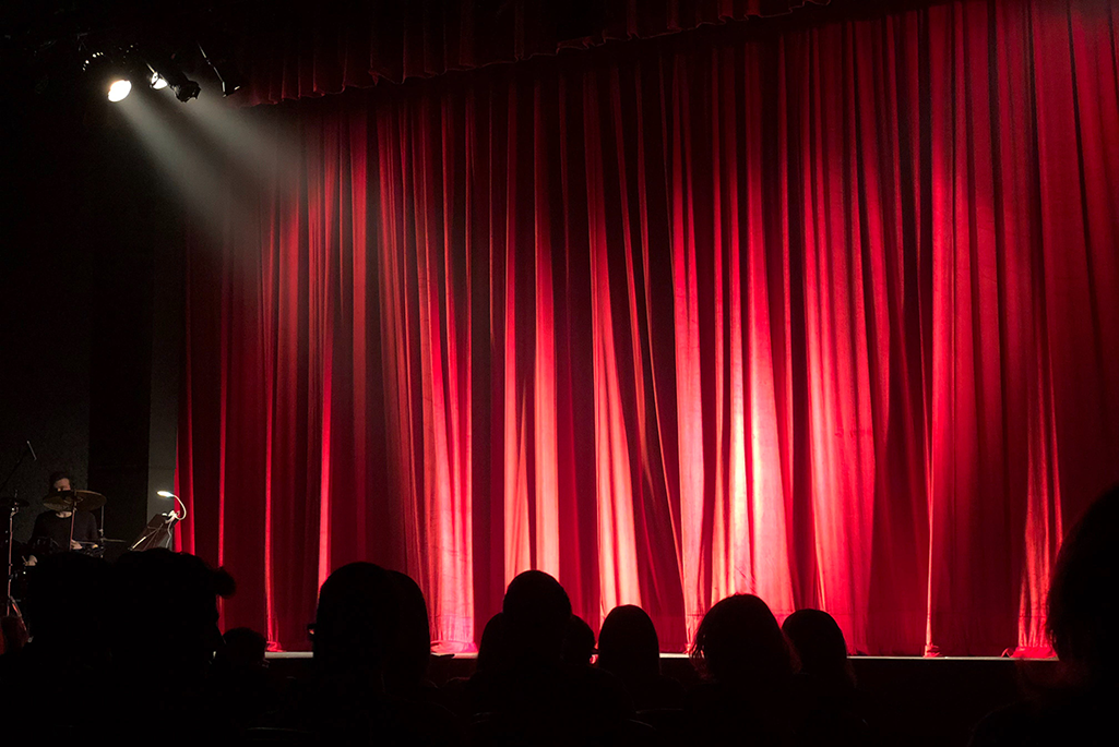 Strålkastare lyser på ett rött draperi framför en scen.